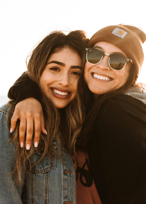 Two females stand with their faces together in an embrace, with big smiles